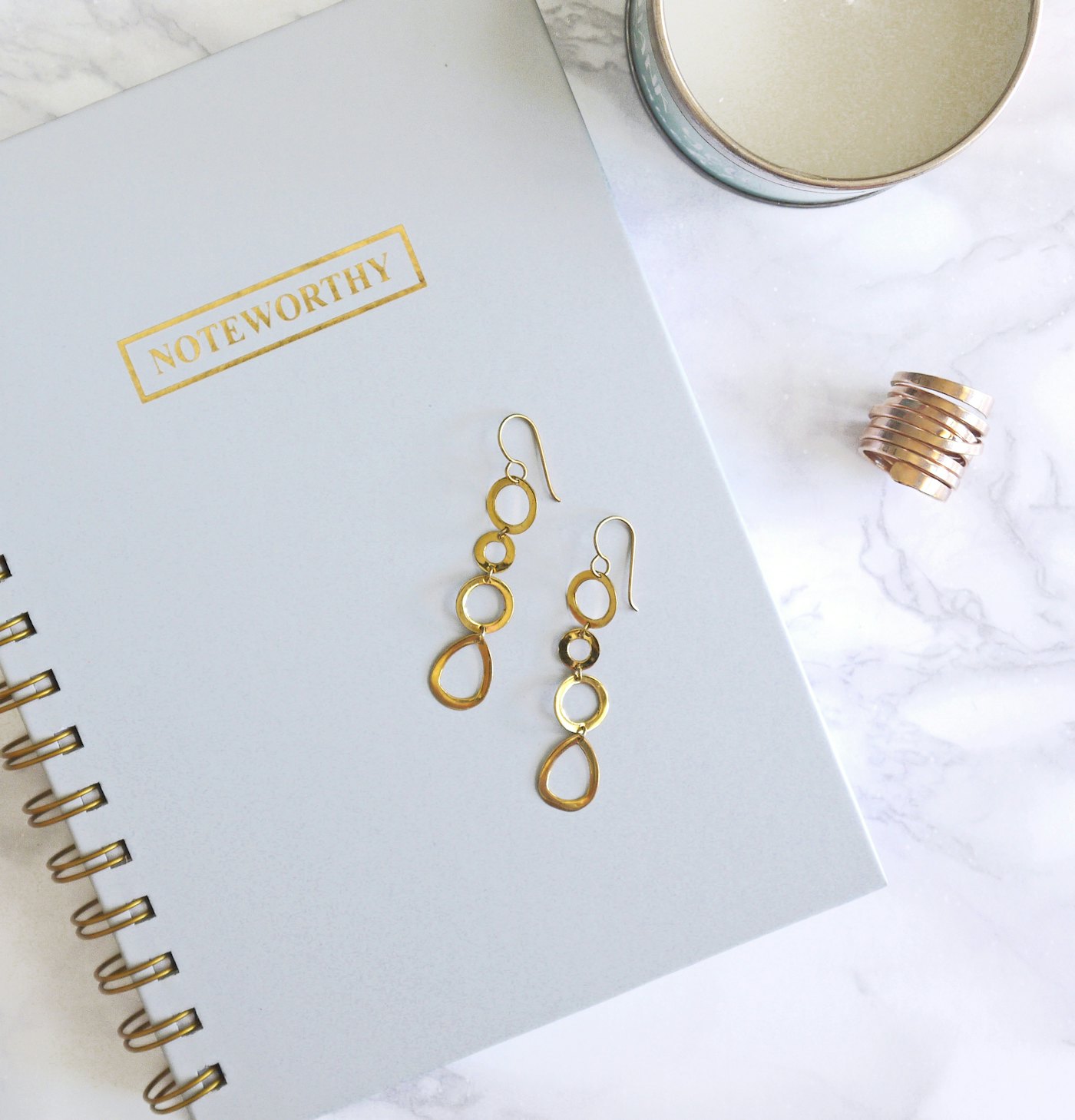 Gold loop earrings resting on a notebook beside a candle