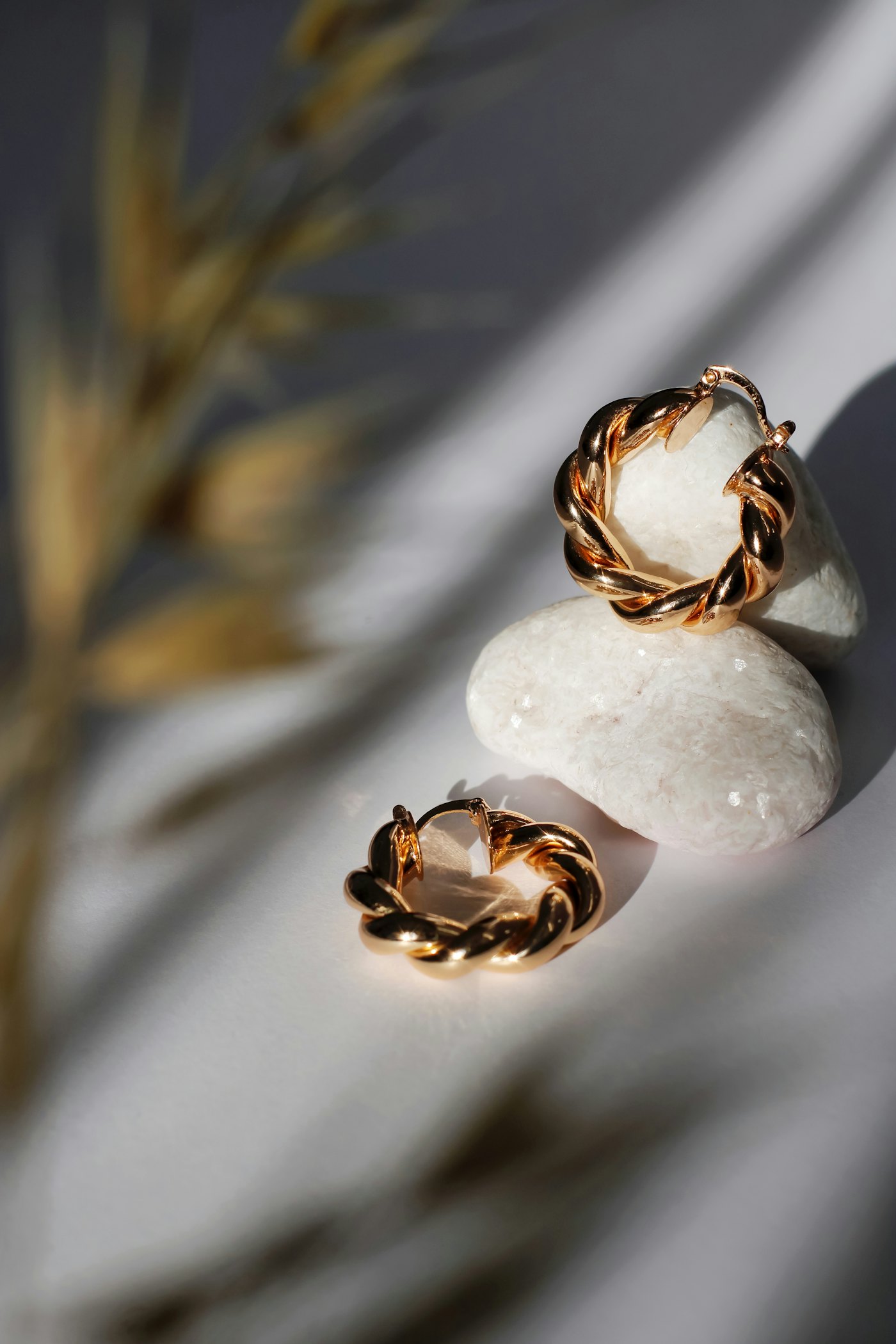 Twisted gold hoop earrings resting on a pale pebble