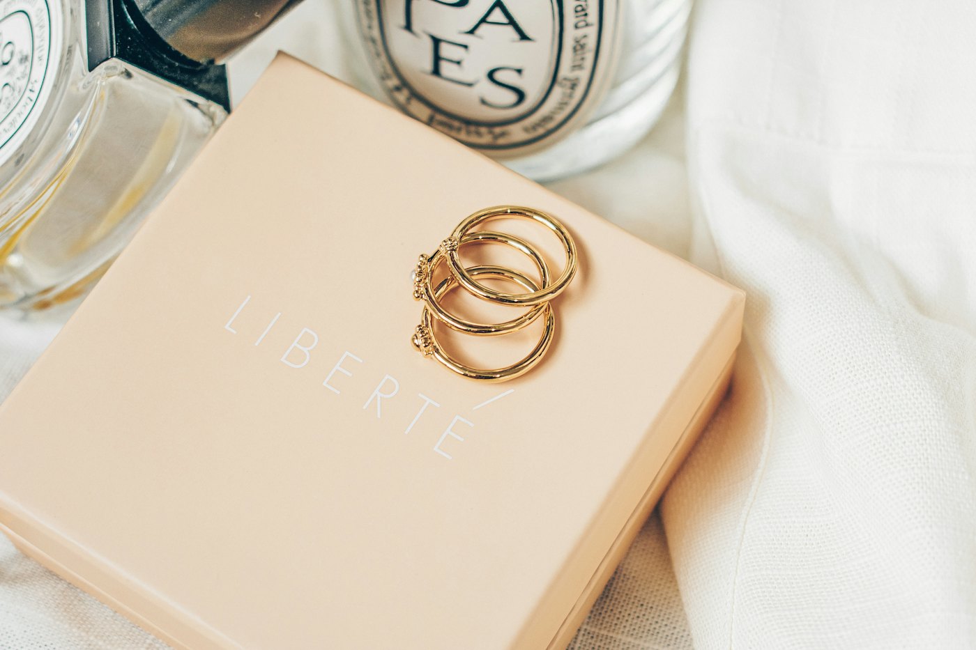 Gold rings resting on a blush gift box beside soft folded paper